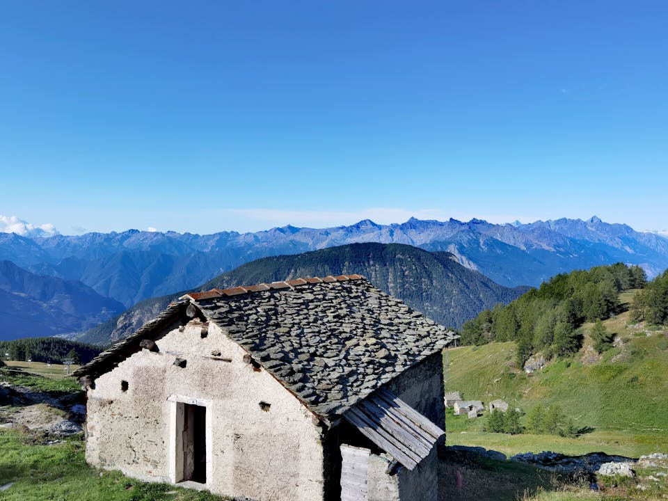 Stone cottage set against a backdrop of majestic mountain ranges under a clear blue sky.