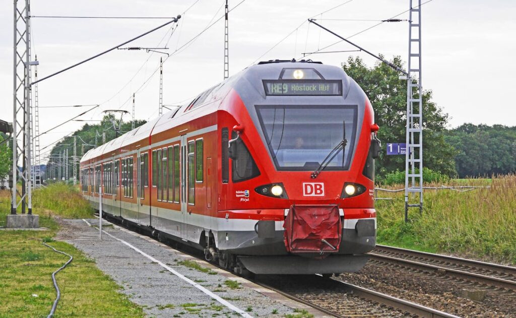 A vibrant red electric train arrives at a rural railway station, showcasing modern public transport.