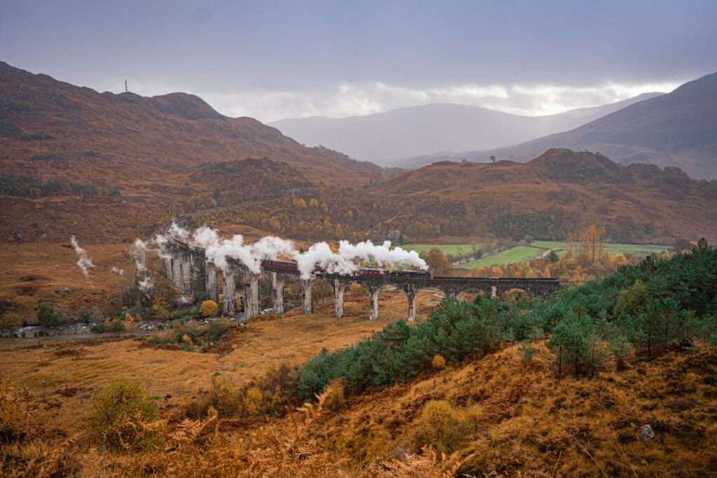 Beautiful landscape of steam train crossing Glenfinnan Viaduct in Scotland during fall.