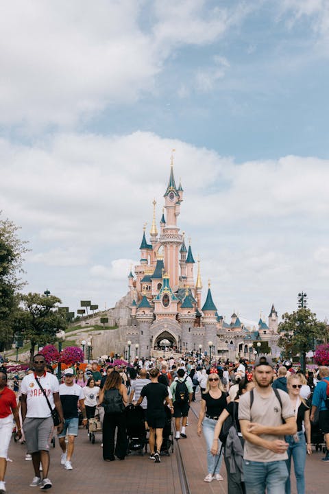 A lively crowd enjoying a day at Disneyland Paris with Sleeping Beauty Castle in view under a bright sky.
