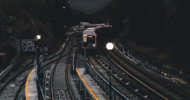 Dramatic nighttime scene of a train approaching a dimly lit station surrounded by mountains and trees.