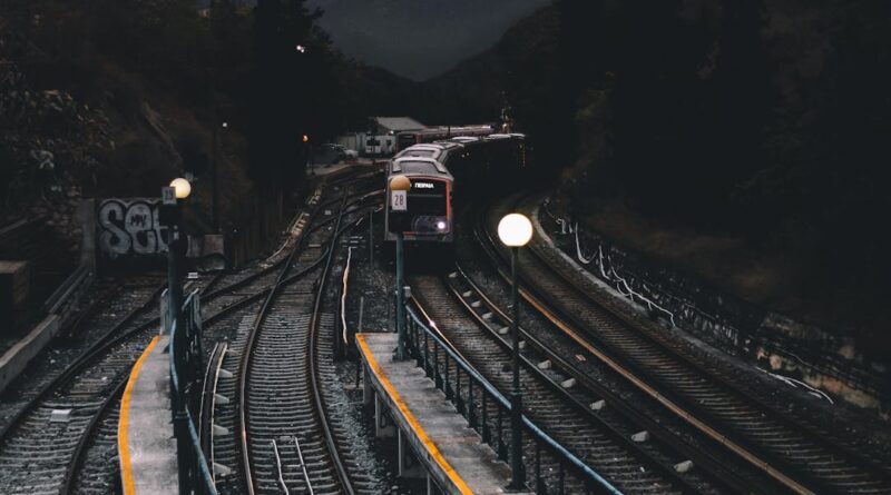 Dramatic nighttime scene of a train approaching a dimly lit station surrounded by mountains and trees.