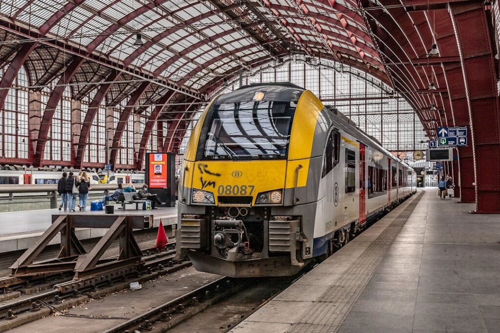 A modern train stops at an indoor railway station terminal with commuters on the platform.