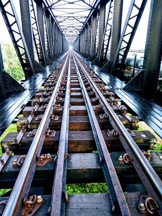 A striking perspective of metal railway tracks through an iron bridge in daylight.
