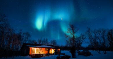 Cabin illuminated under a stunning aurora borealis and starry winter night sky.